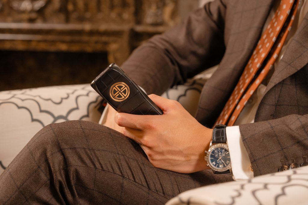 Elegant man holding XOR unique phone with gold emblem and leather finish.