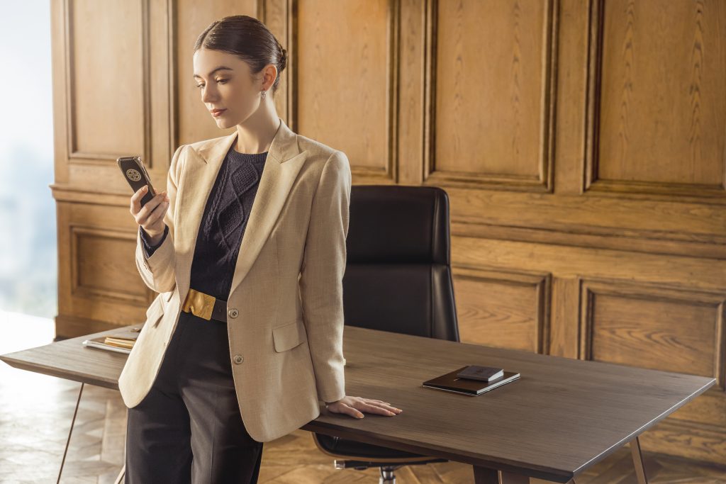 Elegant woman holding XOR phone, the most refined luxury mobile phone in the world, handcrafted in England with 18K gold and alligator leather.